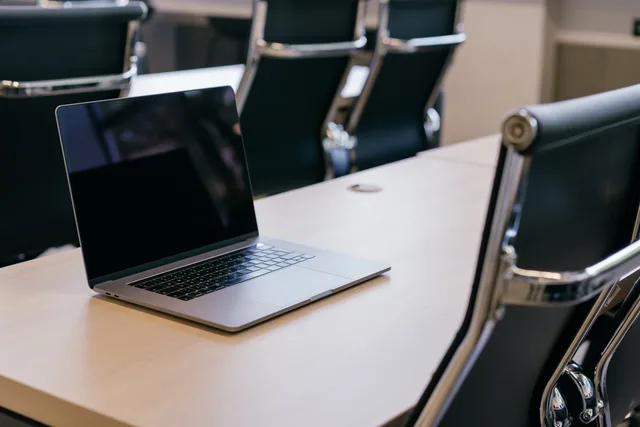 Open laptop on a wooden conference table with stylish black chairs in a modern office setting. Central locations with suburban coworking: compare team fit