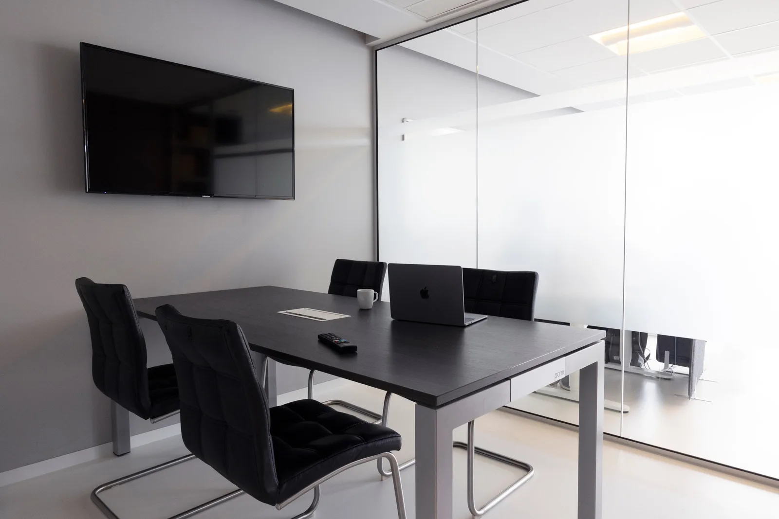 Contemporary meeting room with glass walls, laptop, and television for business discussions.