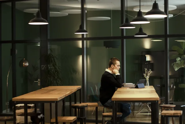 Man focused on work at a modern office with wooden tables and glass panels. Coworking booking systems