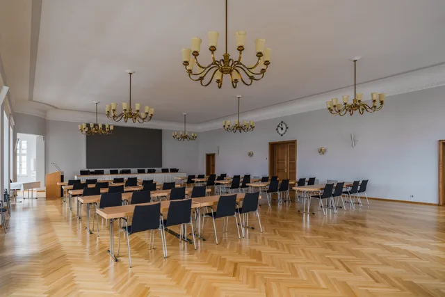 Large meeting room of the Hof town hall. The room can be used for city council and committee meetings. The room contains a number of chairs with matching tables. A display with a resolution of 3840 x 2160 pixels is installed on the wall facing the chairs. A beamer or projector is therefore obsolete. Evaluating meeting rooms before choosing a space